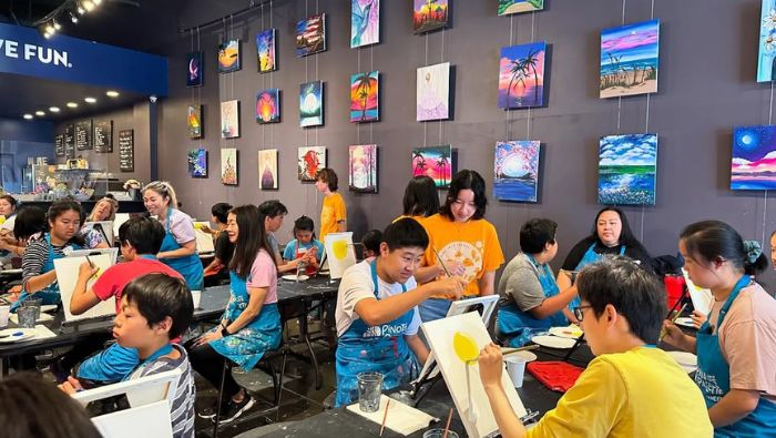 Beckman High School Key Club Painting Palooza 2024: a group of young people paint on canvases; completed paintings hang on the wall behind them