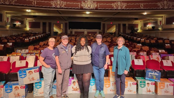 Kiwanis club members stand on the stage of the Strand Theatre. Behind them. every seat is filled with a paper bag containing food donations.