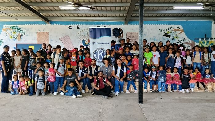 Members of the Kiwanis Club of Mirame pose with students holding backpacks in front of a school mural