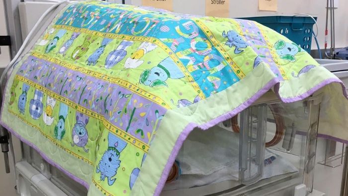 犬や花が描かれた色鮮やかなキルトで覆われたNICUの保育器